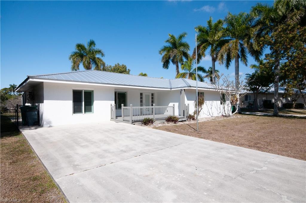 Ranch-style house with stucco siding, a metal roof, a front yard, driveway, and a porch
