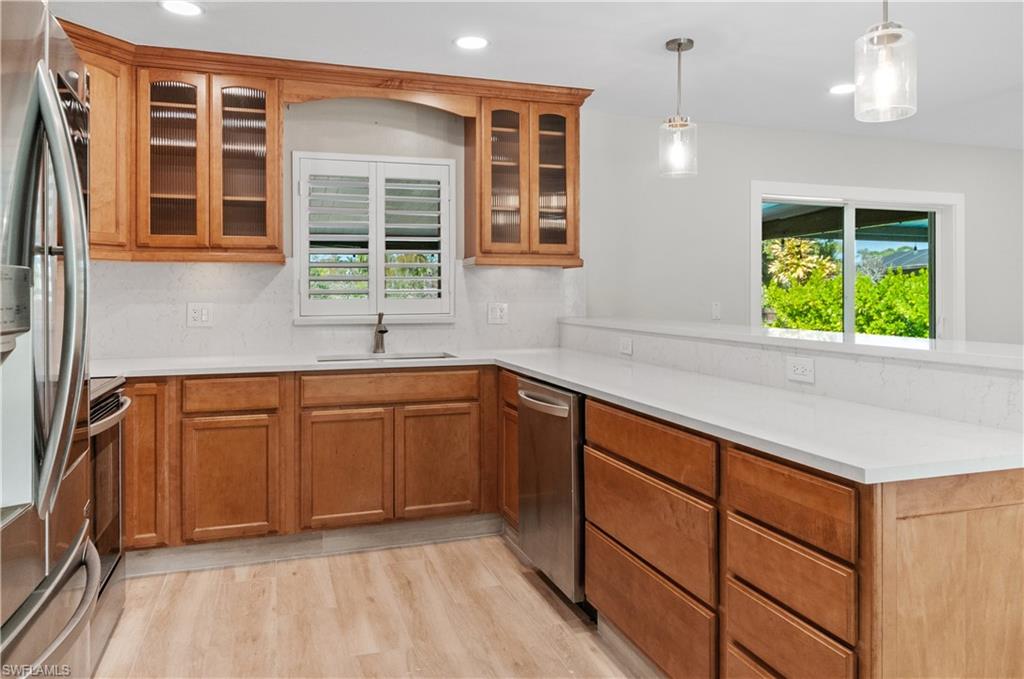Kitchen with wood finish cabinetry, stainless steel appliances, hanging light fixtures, light wood-style floors, and a peninsula