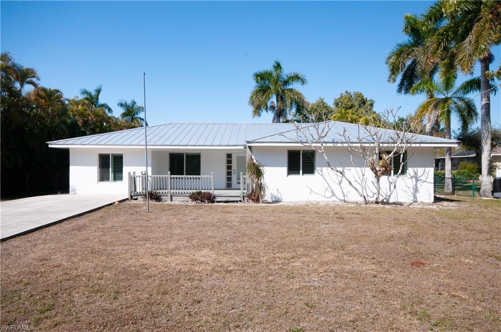 View of front facade with covered porch, a front lawn, stucco siding, and a metal roof
