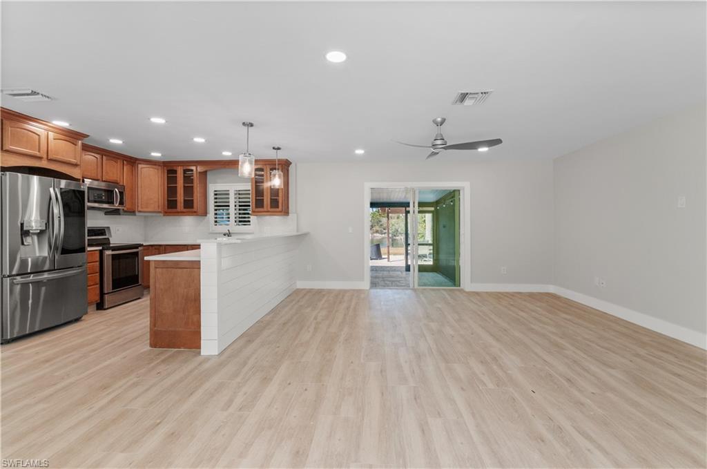 lIVING ROOM OPEN TO Kitchen with stainless steel appliances, glass insert cabinets, wood finish cabinetry, a peninsula, and hanging light fixtures