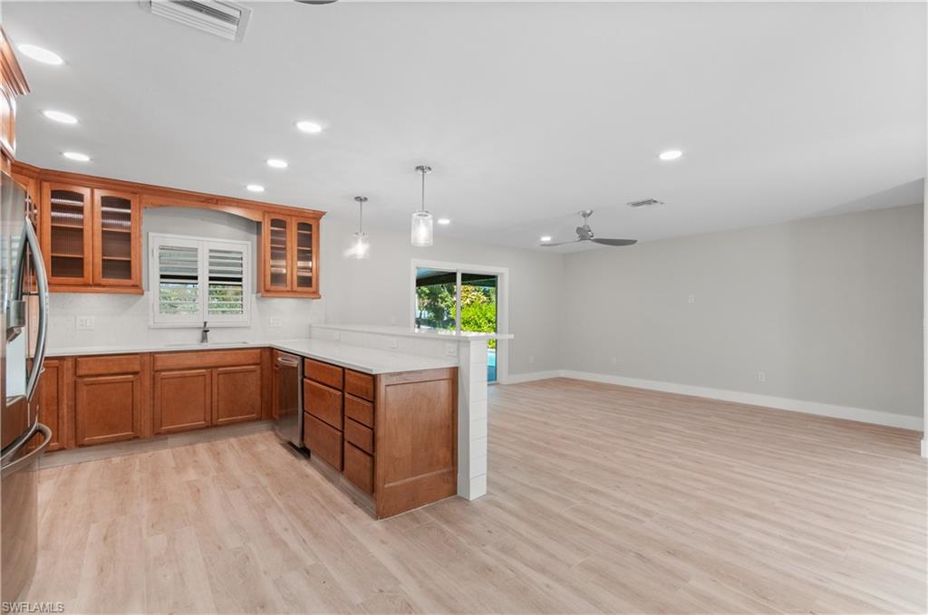 Kitchen featuring glass fronted cabinets, hanging light fixtures, wood finish cabinetry, light wood finished floors, and a peninsula