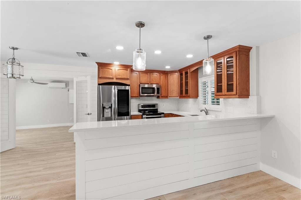 Kitchen featuring hanging light fixtures, glass insert cabinets, a peninsula, light wood finished floors, and stainless steel appliances