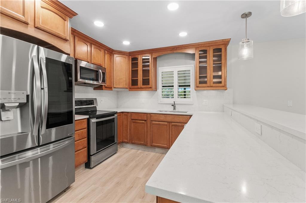 Kitchen with stainless steel appliances, wood finish cabinets, glass insert cabinets, and light wood-style flooring