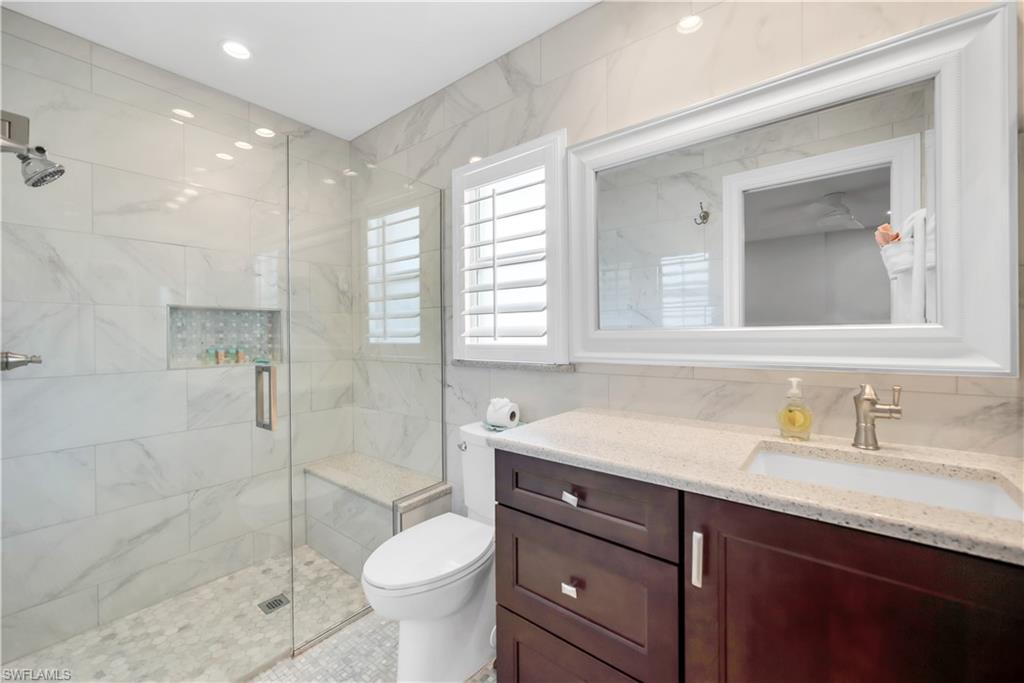 Full bath with a stall shower, toilet, tile walls, and vanity