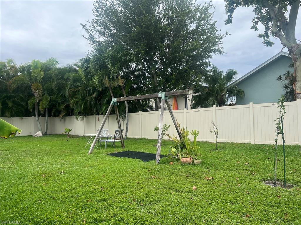 Expansive backyard featuring a green lawn, mature trees, and a light-colored privacy fence