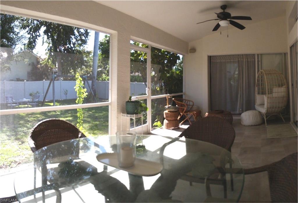 Screened outdoor living space featuring a ceiling fan, tiled flooring, and white privacy fencing beyond the manicured lawn