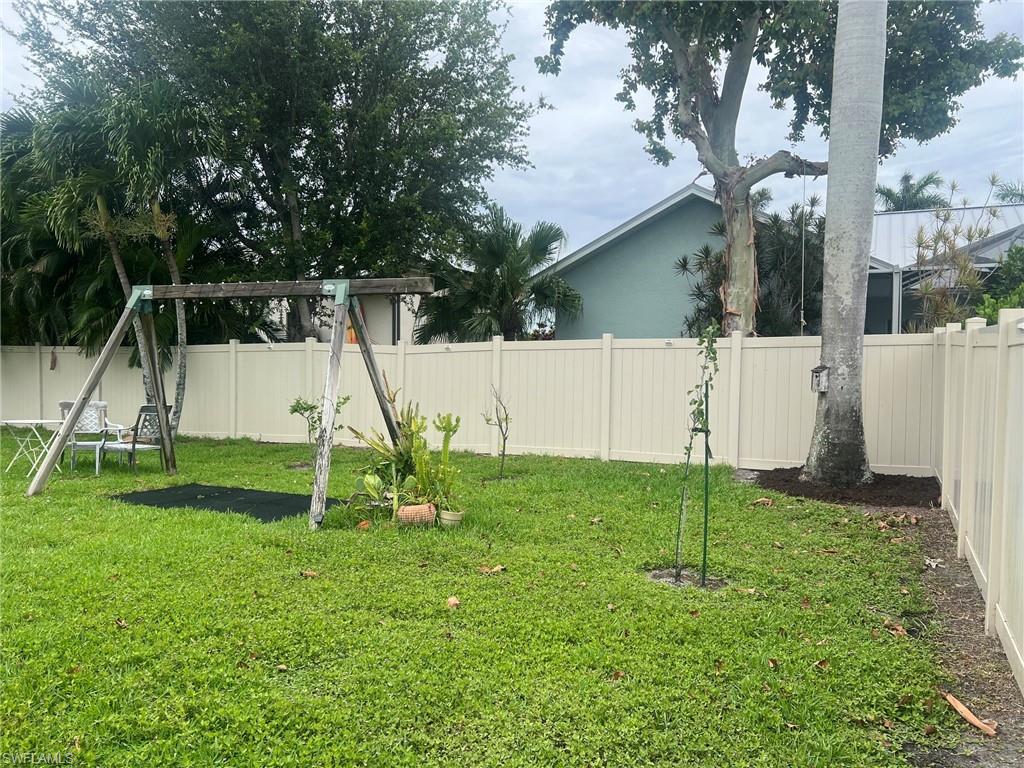 Expansive grassy backyard featuring a full privacy fence, mature trees, and landscaping