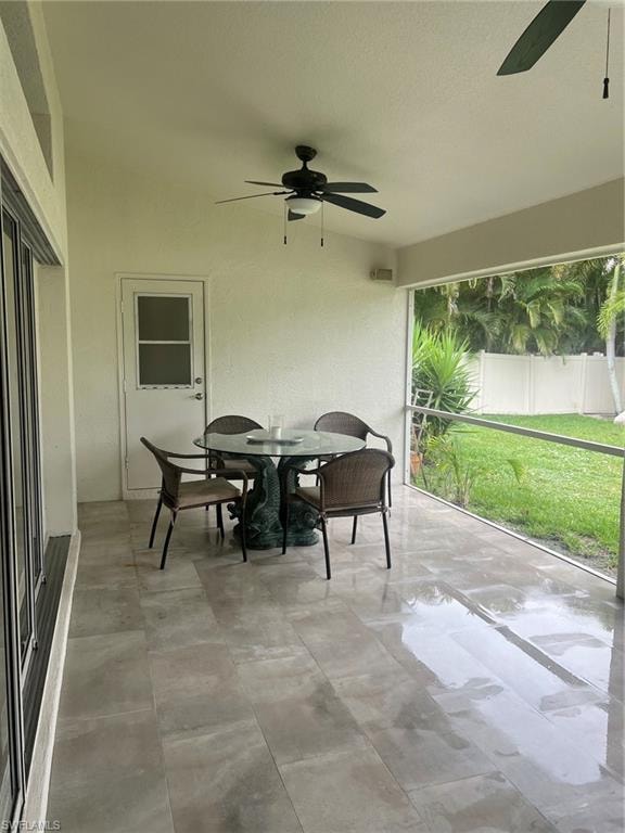 Expansive screened patio featuring large format tile flooring, twin ceiling fans, a white exterior door, and exterior lighting fixtures