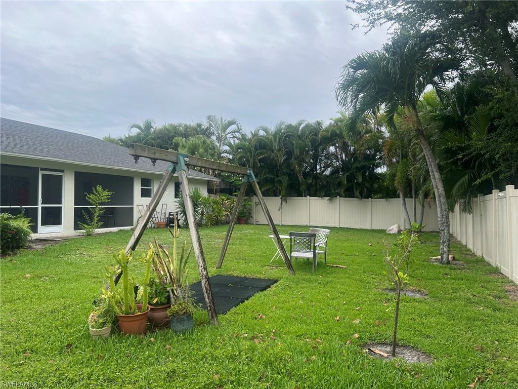 Expansive grassy yard featuring a light-colored privacy fence and mature palm trees
