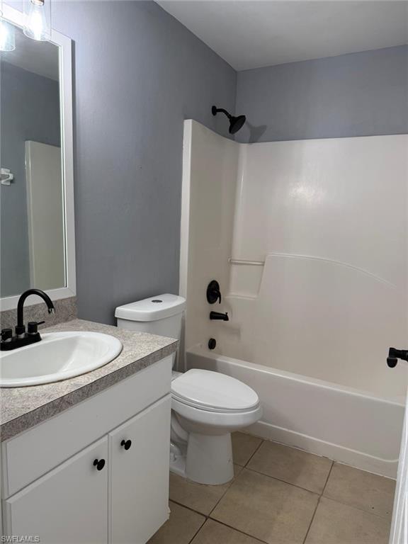 Bathroom featuring a white vanity with a speckled countertop, a white toilet, and a white tub/shower combination with matte black fixtures