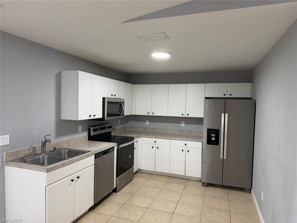Kitchen featuring stainless steel appliances, white cabinetry, light countertops, a double basin sink, and tile flooring