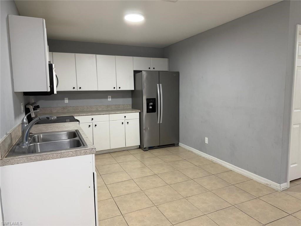 Kitchen featuring white cabinetry, a stainless steel refrigerator, a double basin sink, and tile flooring
