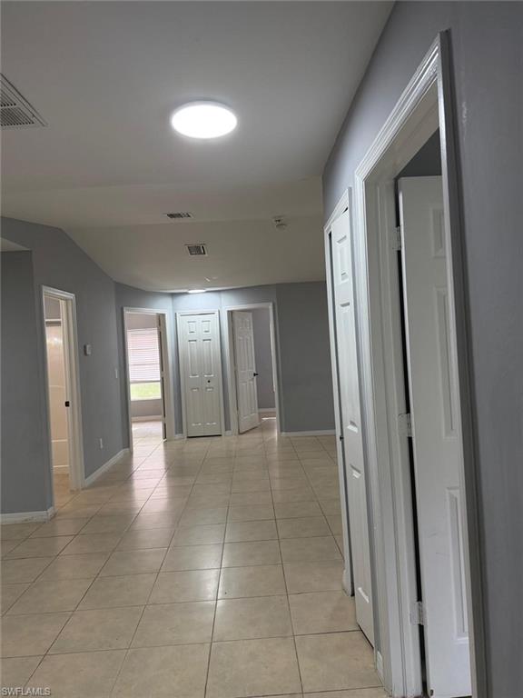 Hallway featuring light-toned tile flooring, light gray wall paint, and multiple white paneled doors