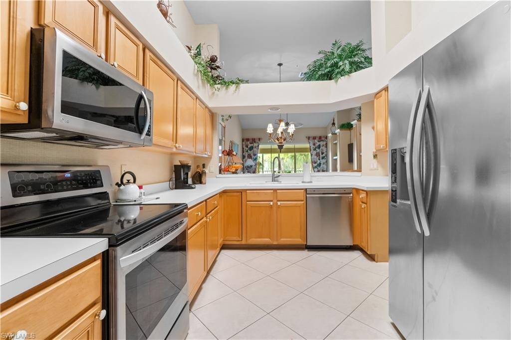 Kitchen with light tile patterned floors, stainless steel appliances, sink, an inviting chandelier, and kitchen peninsula