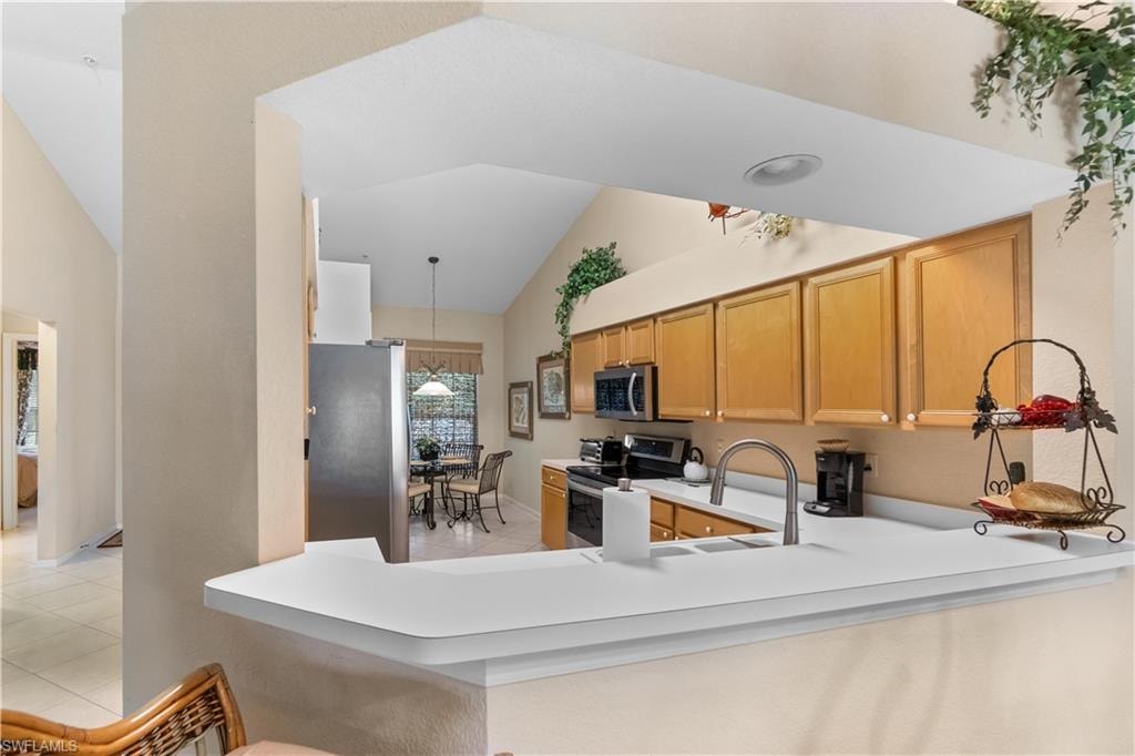 Kitchen featuring light tile patterned floors, stainless steel appliances, sink, lofted ceiling, and kitchen peninsula