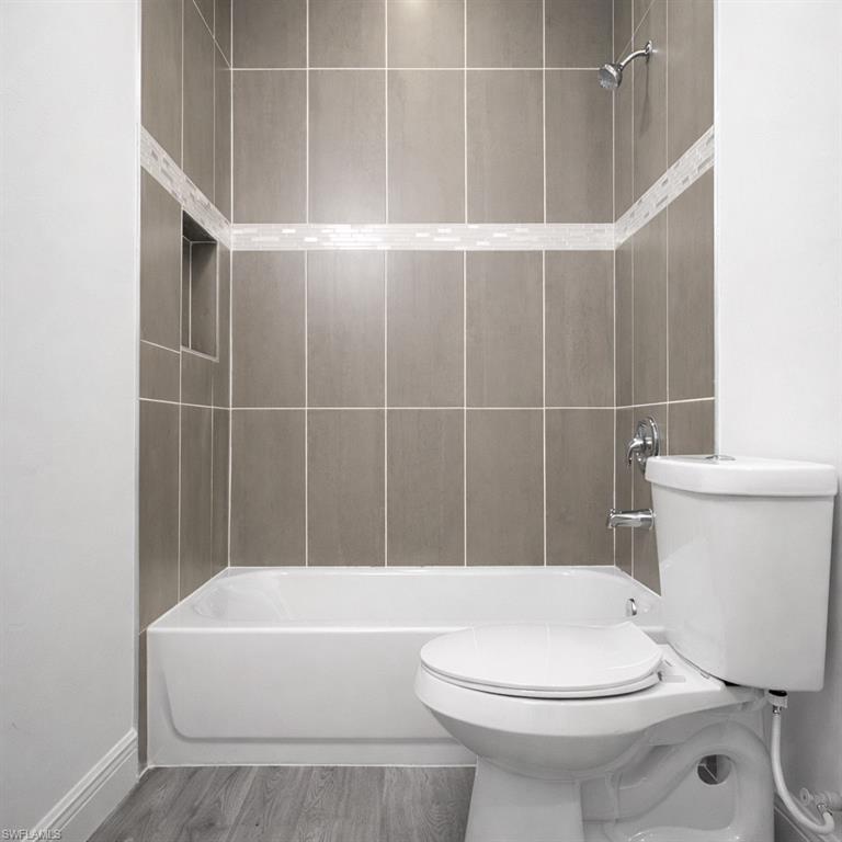 Bathroom featuring a white bathtub, gray rectangular wall tiles with a decorative mosaic accent band, a built-in shower niche, and a chrome shower fixture