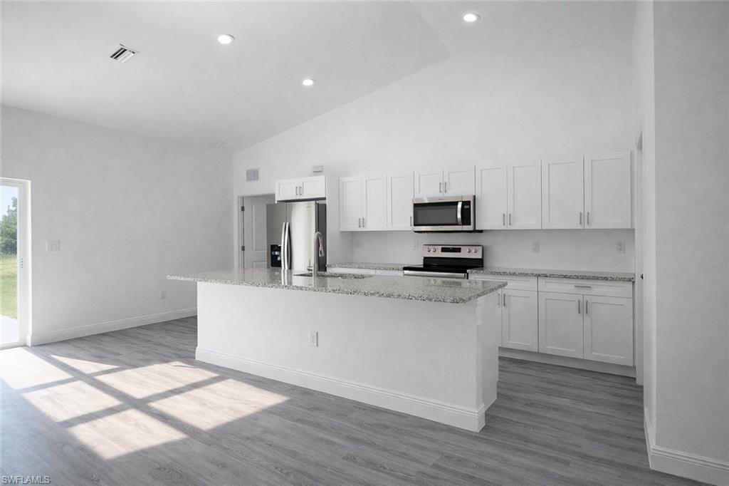 Bright kitchen space featuring white shaker cabinetry, stainless steel appliances, a central island with a granite-style countertop, and wood-finish flooring