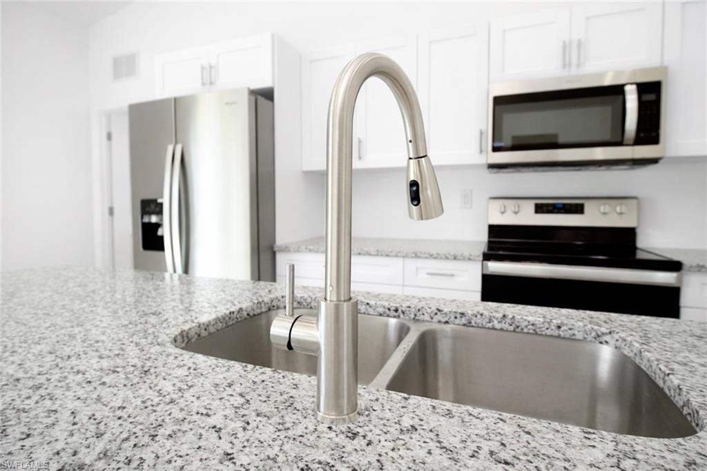 Kitchen featuring a double stainless steel sink with a pull-down faucet, granite countertops, white cabinetry, and stainless steel appliances including a refrigerator, range, and microwave