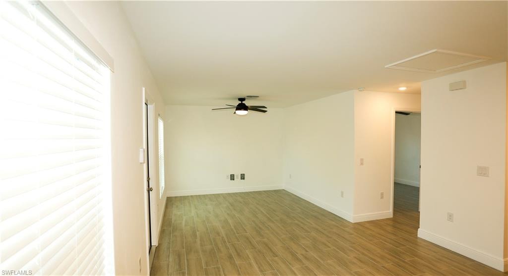 Spacious living area featuring wood-finish flooring, a contemporary ceiling fan with integrated lighting, and multiple windows with blinds