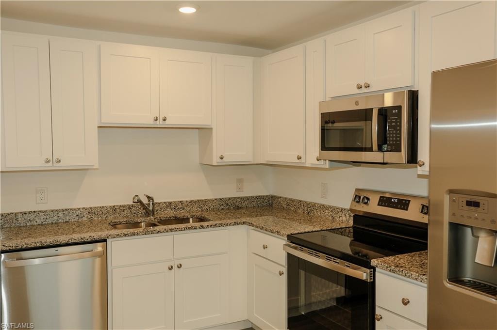 Kitchen featuring white cabinetry, speckled countertops, stainless steel appliances including a refrigerator, built-in microwave, range, and dishwasher