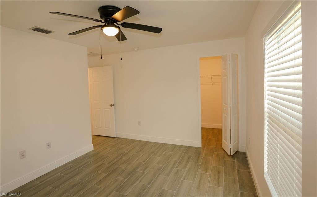Room featuring wood-look tile flooring, a ceiling fan with integrated lighting, a window with horizontal blinds, and a bi-fold closet door revealing shelving