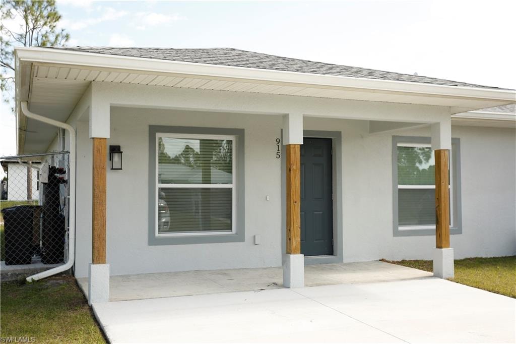 Front exterior featuring a covered porch with natural wood-finish columns, a dark entry door, and light stucco siding with gray trim
