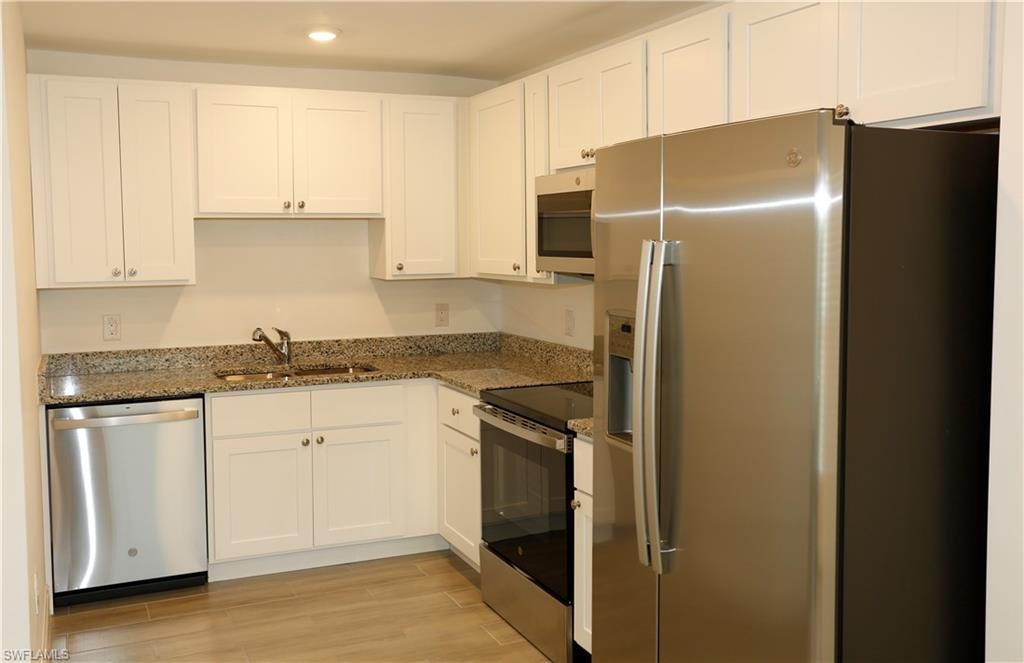 Kitchen featuring white shaker cabinetry, granite countertops, stainless steel appliances, and wood-finish flooring