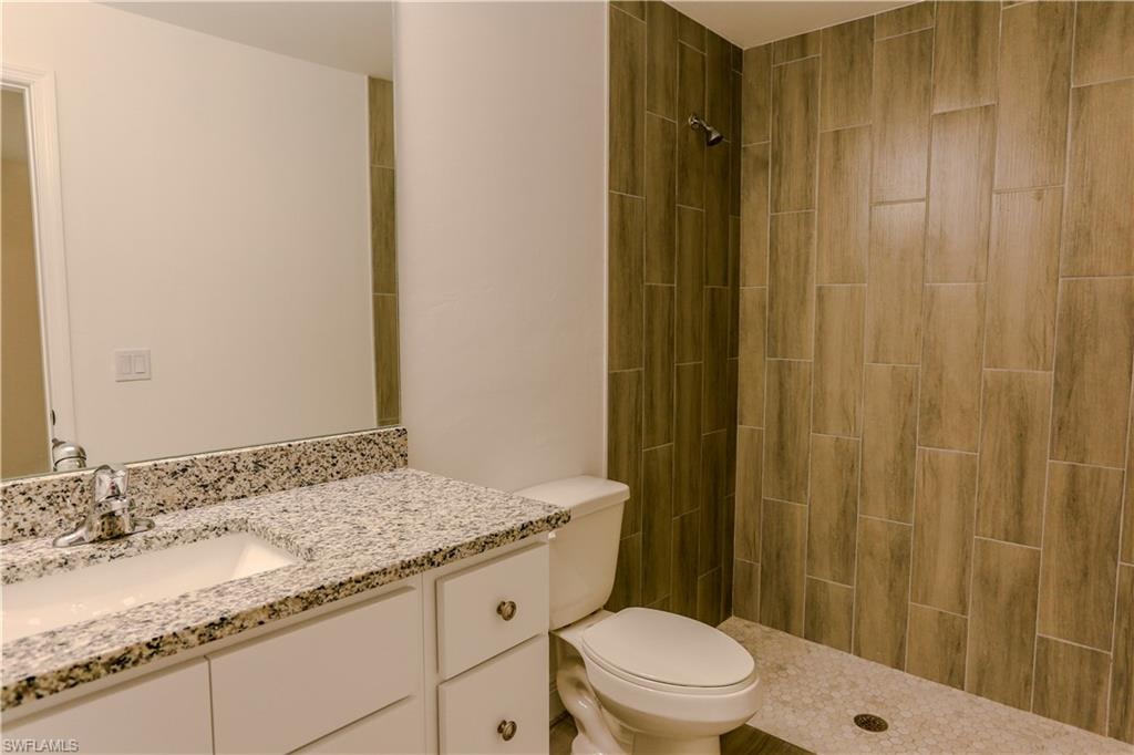 Bathroom featuring a walk-in shower with wood-look plank tiling, a white vanity with a speckled countertop, and an undermount sink