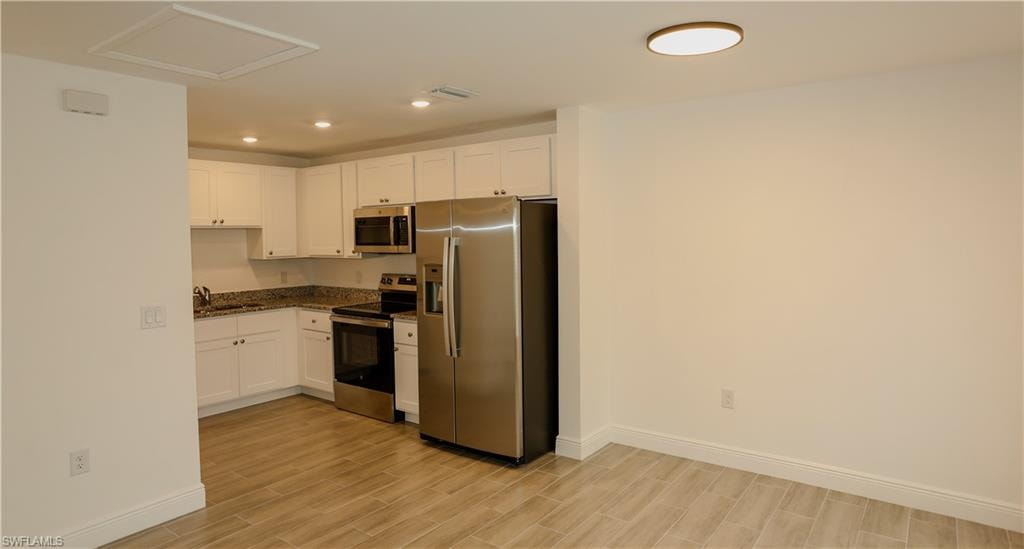 Kitchen featuring white cabinetry, stainless steel appliances, granite countertops, recessed lighting, and wood-finish flooring