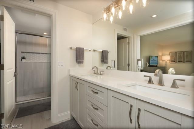 Bathroom featuring double vanity, a stall shower, wood finished floors, and a chandelier