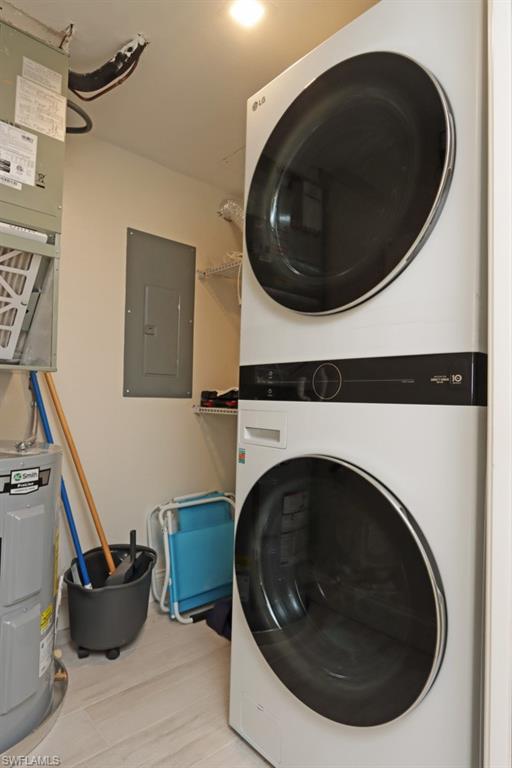 Laundry room featuring stacked washer / dryer, water heater, and electric panel