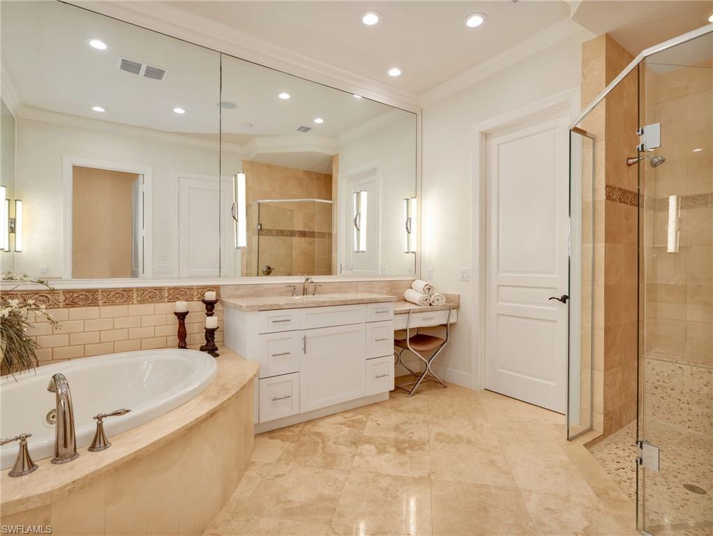 Owner's Suite Bathroom featuring a large jacuzzi tub, a glass-enclosed shower with stone tile, and a full-wall mirror.
