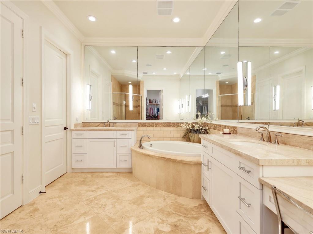 Owner's Suite Bathroom featuring marble flooring, a large corner jacuzzi tub, dual white vanity cabinets with stone countertops, and extensive mirrored wall panels.