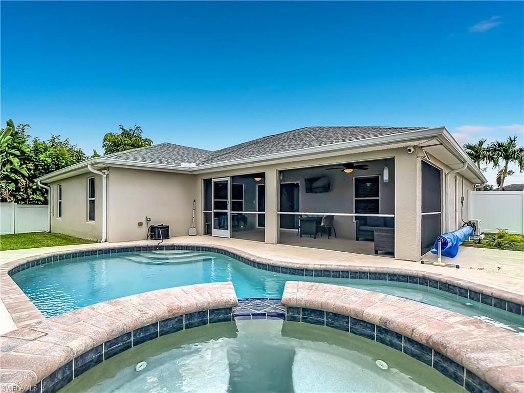 Exterior featuring a curved swimming pool with integrated spa, a screened-in patio, and a light-colored stucco finish