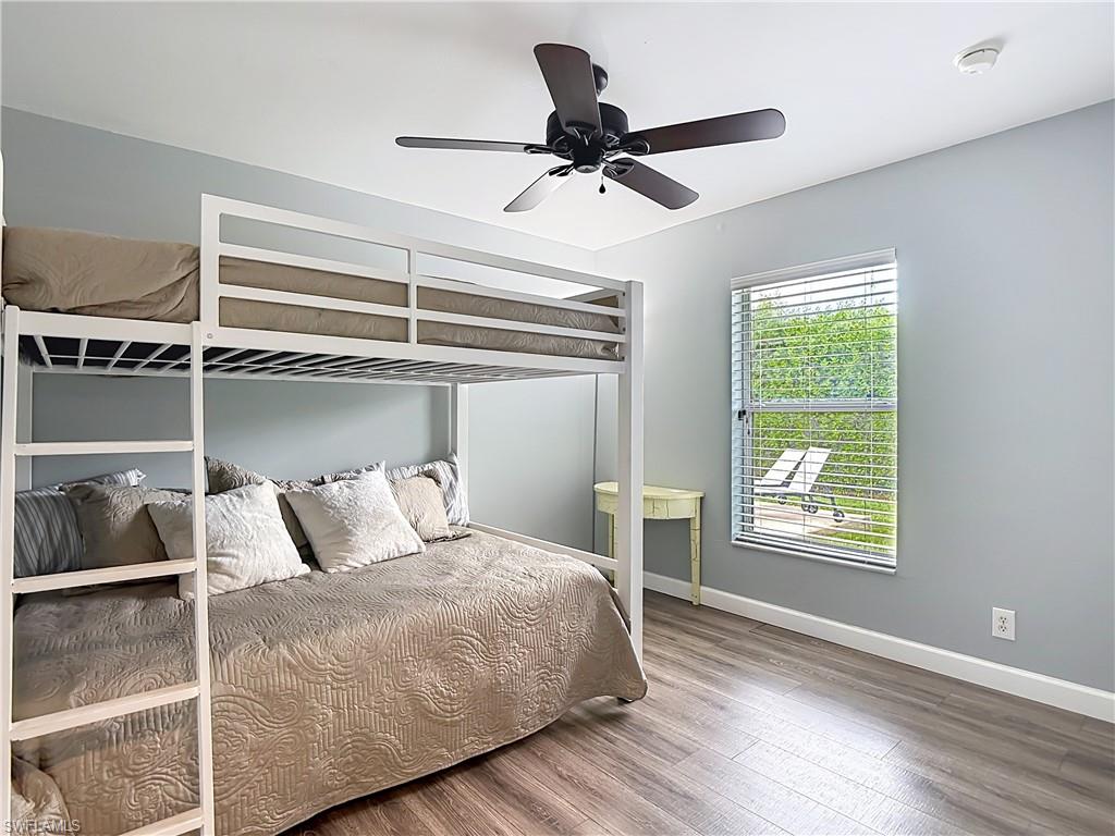 Room featuring wood-finish flooring, light gray walls, a window with horizontal blinds, and a dark-toned ceiling fan