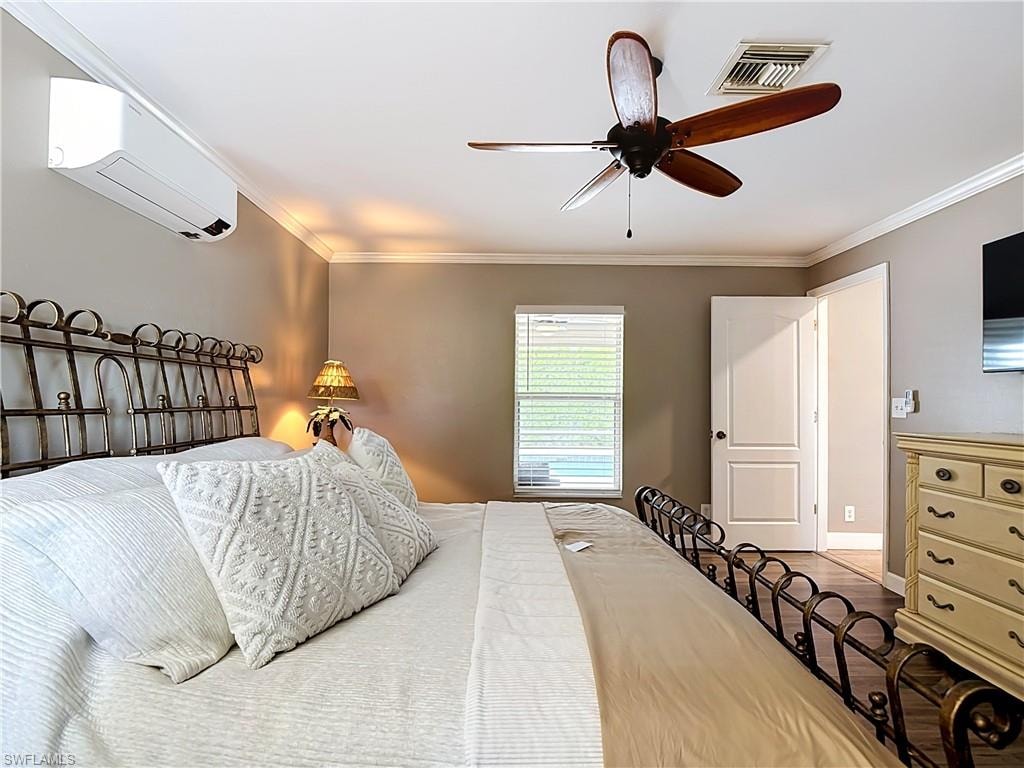 Bedroom featuring a wall-mounted mini-split system and a ceiling fan with wood-finish blades
