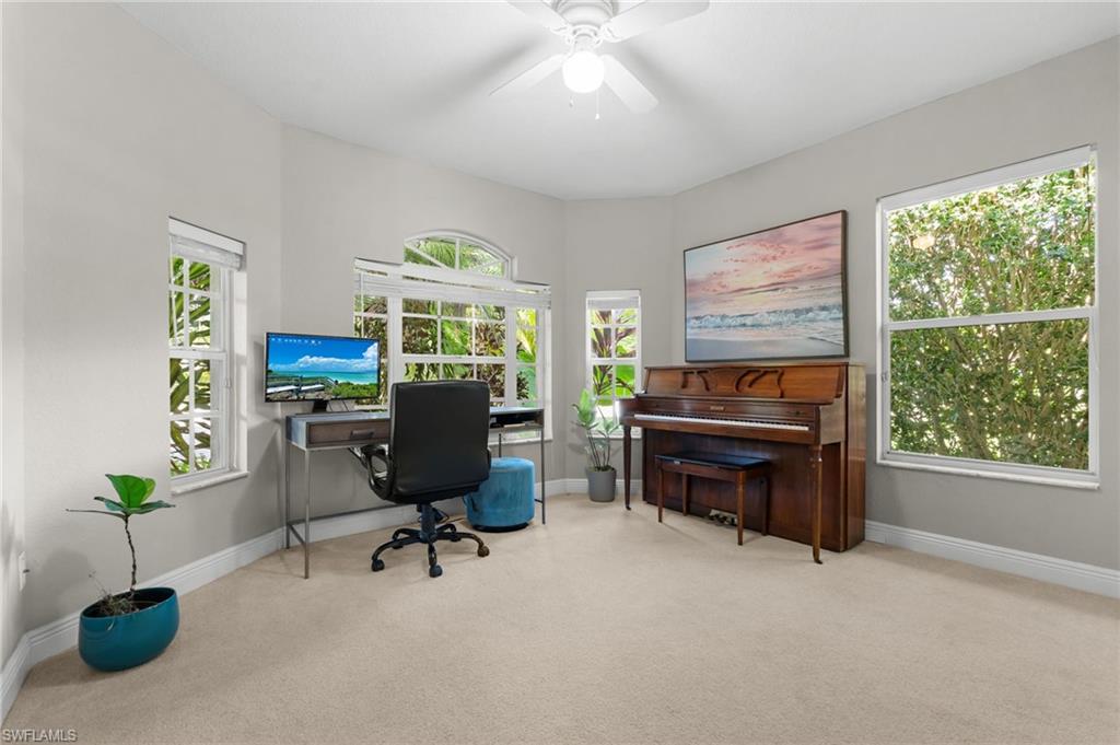 Spacious room featuring neutral carpeting, light gray walls, a white ceiling fan, and multiple windows providing natural illumination