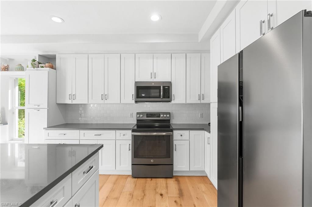 Modern kitchen featuring white shaker cabinetry, stainless steel appliances, dark countertops, a subway tile backsplash, and light wood-finish flooring