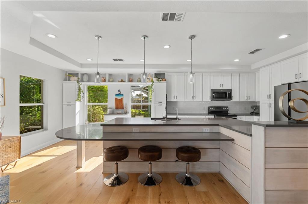 Kitchen featuring a large central island with seating, white shaker cabinetry, stainless steel appliances, and wood-finish flooring