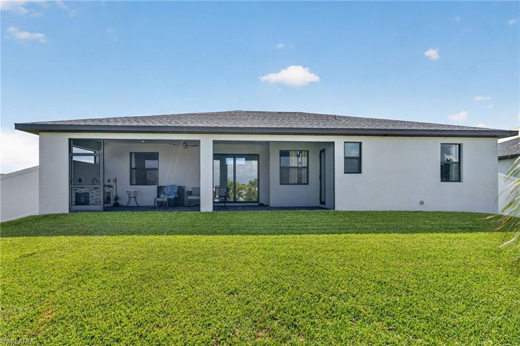 Expansive green lawn with a contemporary single-story home featuring a covered patio, screened-in outdoor kitchen, and dark-framed windows