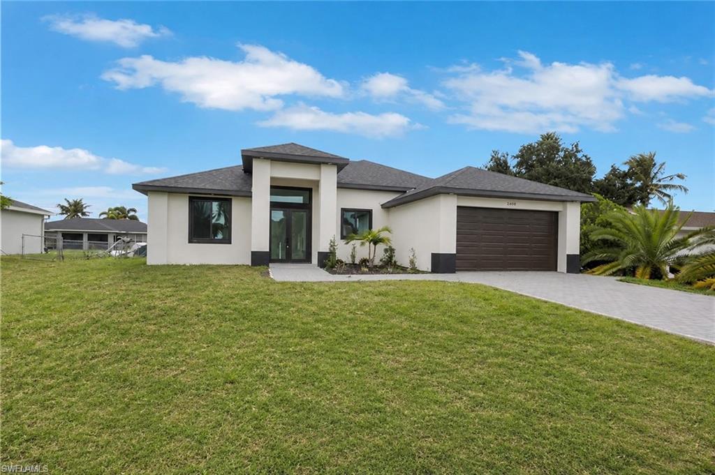 Contemporary stucco exterior with a dark shingle roof, integrated two-car garage, paver driveway, and a manicured lawn