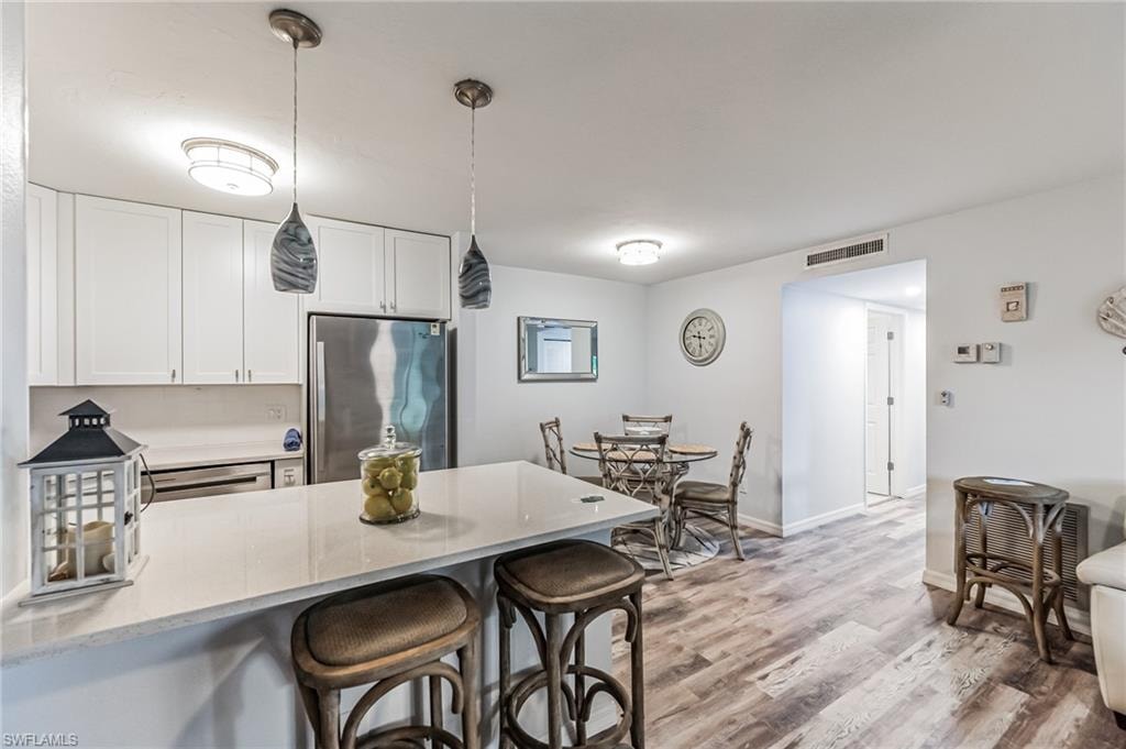 Modern kitchen featuring white shaker cabinetry, stainless steel appliances, a breakfast bar with pendant lighting, and wood-finish flooring