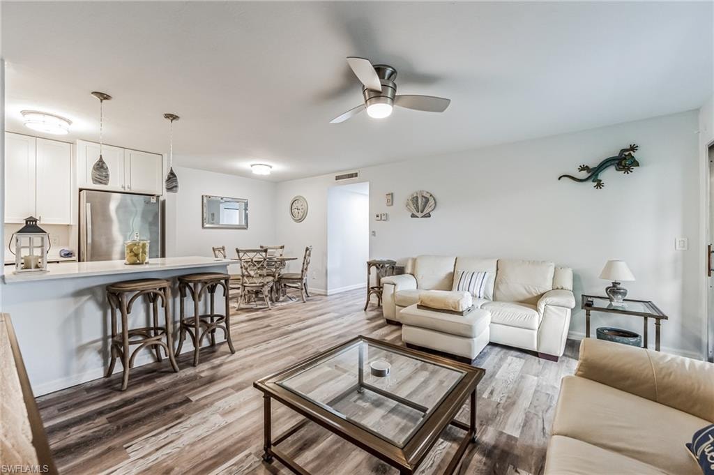 Open-concept living space featuring wood-finish flooring, a kitchen with white cabinetry and stainless steel appliances, a breakfast bar with pendant lighting, and a dining area with a round table