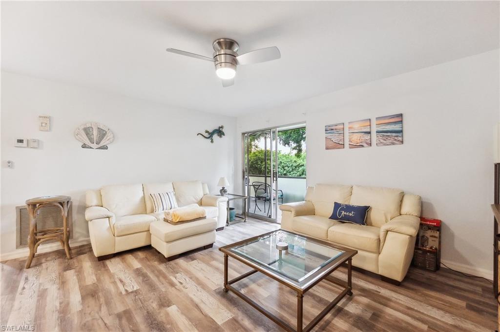 Bright living area featuring wood-finish flooring, a contemporary ceiling fan with integrated lighting, and a sliding glass door opening to a private balcony