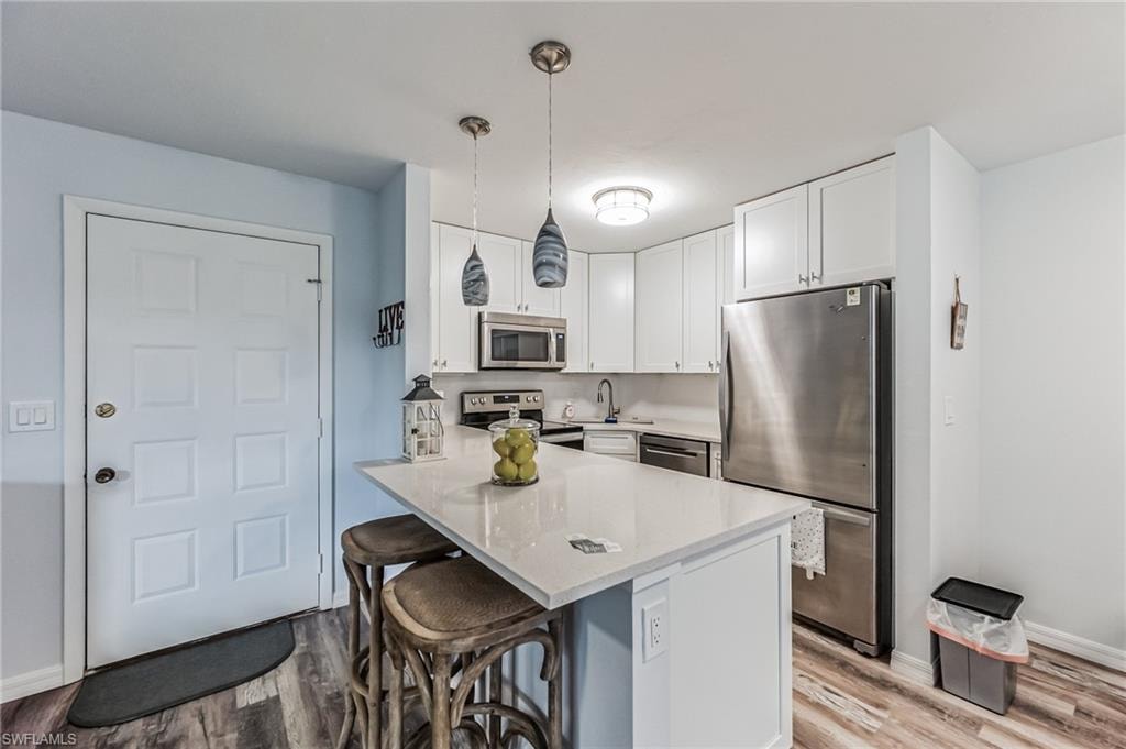 Modern kitchen featuring a central island with countertop seating, white cabinetry, stainless steel appliances, and wood-finish flooring