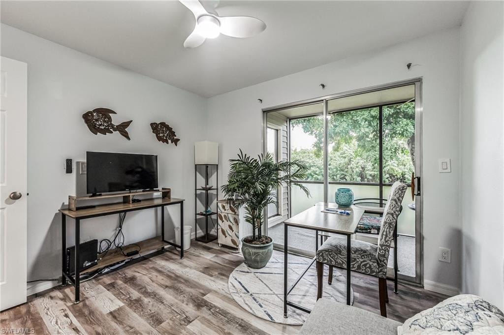 Living area featuring wood-finish flooring, a ceiling fan, and sliding glass doors opening to an outdoor patio with surrounding trees