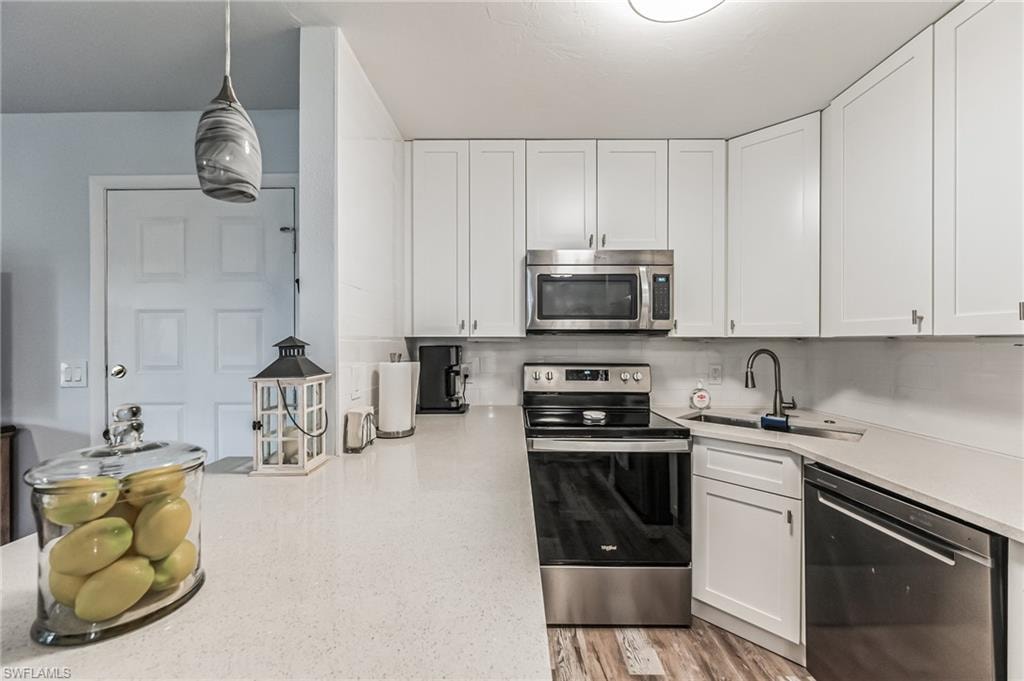 Modern kitchen featuring white cabinetry, light-toned countertops, stainless steel appliances, a corner sink with a gooseneck faucet, and wood-finish flooring