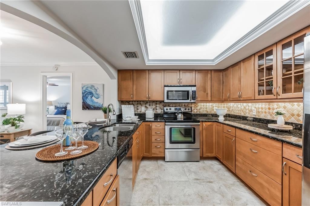 U-shaped kitchen featuring wood cabinetry, dark stone countertops, stainless steel appliances, and a tiled backsplash