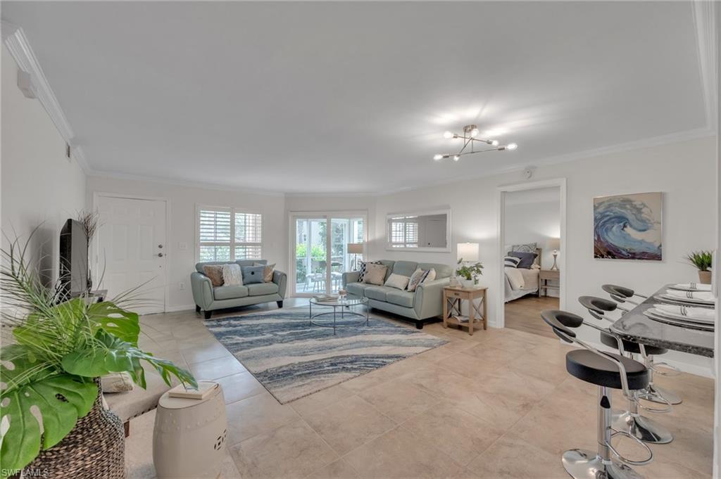 Bright open-concept living area featuring tile flooring, crown molding, and a modern chandelier
