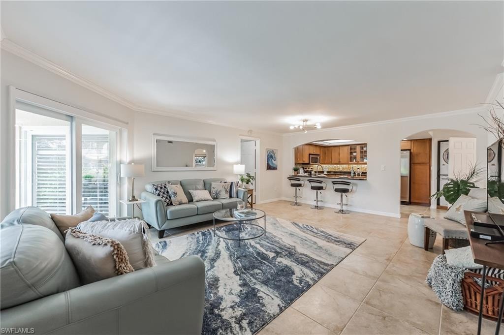 Spacious living area featuring tile flooring, crown molding, a kitchen pass-through with breakfast bar, dual French doors, and an arched doorway